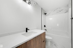 Contemporary bathroom featuring a wood-finish vanity with a white countertop and integrated sink, matte black faucet, and a wall-mounted light fixture - 
