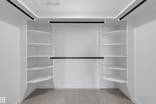 Spacious walk-in closet featuring white built-in shelving, multiple hanging rods, and light gray carpet flooring - 30 Elsinore Place, Edmonton, AB 