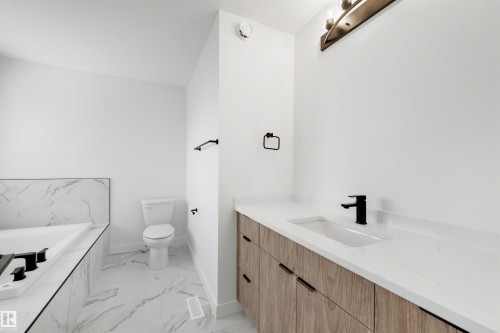 Bathroom featuring a built-in tub with tile surround, a toilet, and a vanity with a white countertop and wood-finish cabinetry - 30 Elsinore Place, Edmonton, AB 