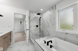Bathroom featuring large-format marble-look tile flooring, matching wall tile in the shower surround, a built-in soaking tub with matte black fixtures, and a glass-enclosed shower with a rainfall showerhead - 
