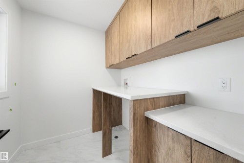 Laundry area featuring light wood-finish cabinetry, white countertops, and light tile flooring - 30 Elsinore Place, Edmonton, AB 