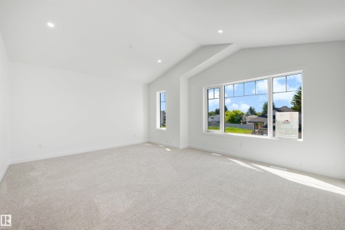 Spacious room featuring vaulted ceilings, recessed lighting, neutral carpeting, and a large window with multiple panes - 30 Elsinore Place, Edmonton, AB 