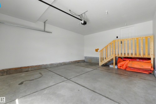 Spacious garage with concrete flooring, painted white walls, and a wood staircase providing interior access - 30 Elsinore Place, Edmonton, AB 