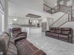 Spacious living area featuring polished tile flooring, a two-story ceiling, and a prominent staircase with dark wood railings and metal balusters - 