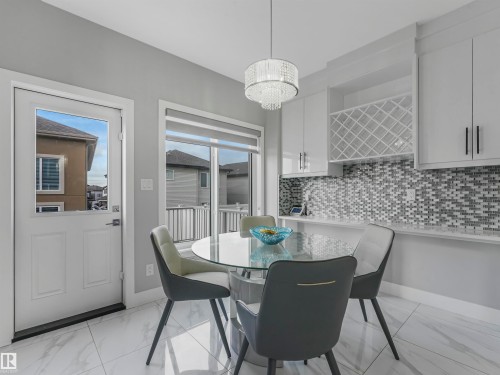 Modern kitchen and dining area featuring sleek white cabinetry, a stylish mosaic tile backsplash, and a contemporary chandelier - 2412 14 Avenue, Edmonton, AB 