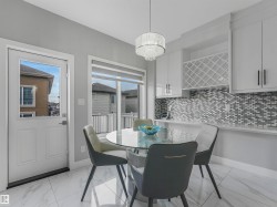 Modern kitchen and dining area featuring sleek white cabinetry, a stylish mosaic tile backsplash, and a contemporary chandelier - 