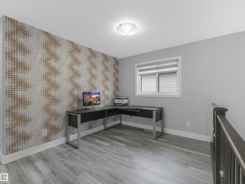 Spacious room featuring patterned accent wall, light gray walls, wood-finish flooring, a window with horizontal blinds, and a contemporary ceiling light fixture - 2412 14 Avenue, Edmonton, AB 