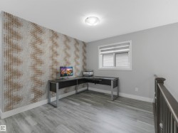 Spacious room featuring patterned accent wall, light gray walls, wood-finish flooring, a window with horizontal blinds, and a contemporary ceiling light fixture - 