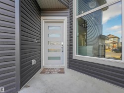 Contemporary grey siding exterior with a light grey entry door featuring horizontal glass inserts, framed by a wide white trim - 
