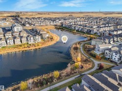 Residential community featuring a prominent central pond, paved pathways, and multiple single-family homes with gray roofs - 