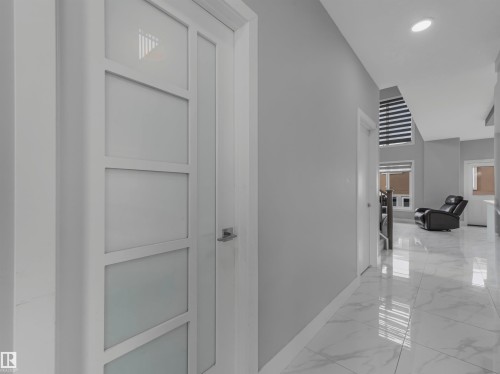 Hallway featuring a contemporary white panel door with frosted glass inserts, recessed ceiling lighting, glossy marble-look tile flooring, and a window with horizontal blinds - 2412 14 Avenue, Edmonton, AB 