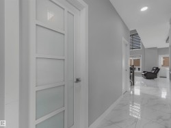 Hallway featuring a contemporary white panel door with frosted glass inserts, recessed ceiling lighting, glossy marble-look tile flooring, and a window with horizontal blinds - 