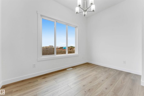 Bright interior space featuring a large three-panel window, light wood-finish flooring, and crisp white walls - 1972 210 Street, Edmonton, AB 