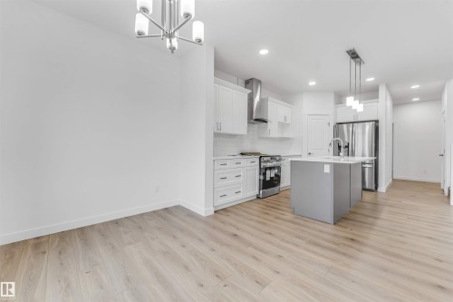 Modern kitchen featuring a gray island with integrated sink, stainless steel appliances, white cabinetry, and light wood-finish flooring throughout - 1972 210 Street, Edmonton, AB 