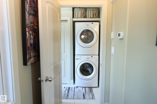 Dedicated laundry closet featuring a stackable washer and dryer, tile flooring, and integrated shelving - 7492 May Common, Edmonton, AB 