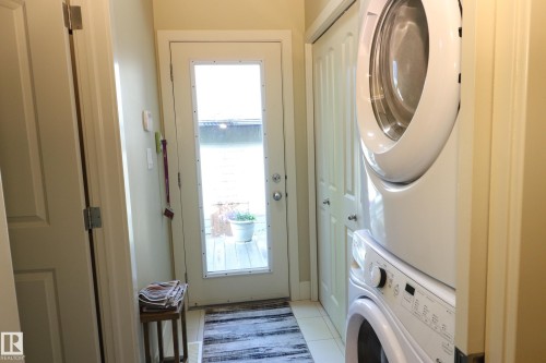 Dedicated laundry area featuring a white stacked washer and dryer, tile flooring, and a full-light exterior door - 7492 May Common, Edmonton, AB 