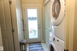 Dedicated laundry area featuring a white stacked washer and dryer, tile flooring, and a full-light exterior door - 