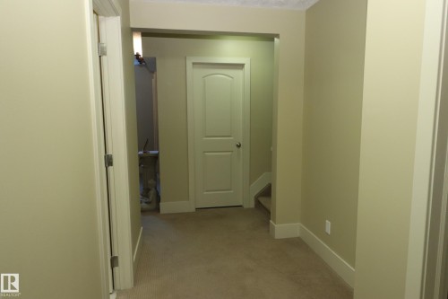 Carpeted hallway featuring light-toned walls, white trim, and a prominent arched door frame - 7492 May Common, Edmonton, AB 