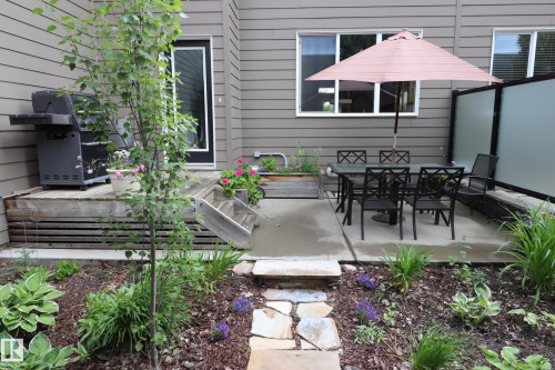 Exterior patio space featuring a concrete pad with privacy screen, a separate wooden deck, and a stone paver pathway - 7492 May Common, Edmonton, AB 