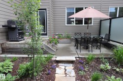 Exterior patio space featuring a concrete pad with privacy screen, a separate wooden deck, and a stone paver pathway - 