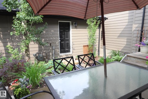 Patio area featuring a glass-top table, integrated umbrella, and surrounding landscaping - 7492 May Common, Edmonton, AB 
