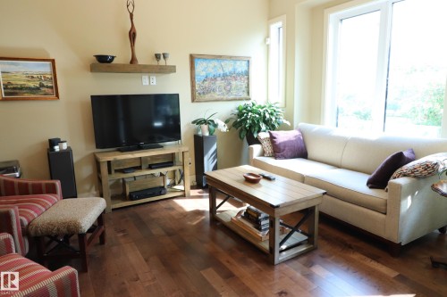 Spacious living area featuring wood-finish flooring, ample natural light from large windows, and neutral wall tones - 7492 May Common, Edmonton, AB 