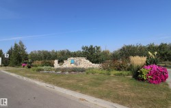 Landscaped entrance featuring a stone-look wall, vibrant flowering plants, ornamental grasses, and mature trees - 
