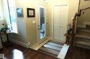 Entryway featuring a full-light exterior door, rich wood-finish flooring, a bi-fold closet, and a carpeted staircase with a wood railing - 7492 May Common, Edmonton, AB 