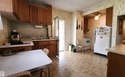 Kitchen featuring wood cabinetry, a tiled backsplash, and patterned wallpaper - 9522 110 Avenue Nw, Edmonton, AB - Indoor Photo Showing Kitchen