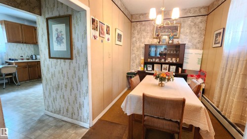 Dining area featuring a central chandelier, wood paneling, and patterned wallpaper - 9522 110 Avenue Nw, Edmonton, AB - Indoor Photo Showing Dining Room