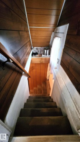 Carpeted staircase with wood paneling and a wooden handrail, featuring a small window at the landing - 9522 110 Avenue Nw, Edmonton, AB - Indoor Photo Showing Other Room