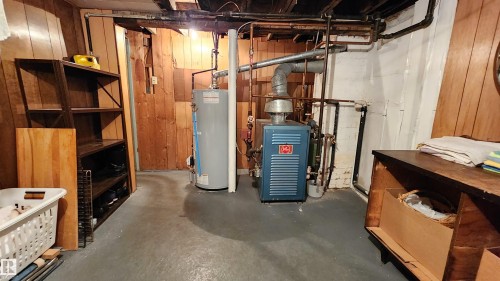 Utility space featuring a water heater and boiler system, exposed plumbing, and wood paneling - 9522 110 Avenue Nw, Edmonton, AB - Indoor Photo Showing Basement