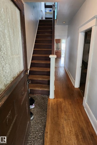 Entryway featuring a wood-panel door with decorative glass, wood-finish flooring extending into a corridor, and a staircase with wood treads and a white newel post - 9522 110 Avenue Nw, Edmonton, AB - Indoor Photo Showing Other Room
