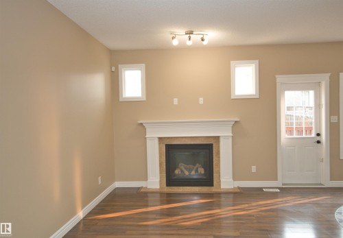 Living area featuring wood-finish flooring, a white trim gas fireplace with a tiled surround, and track lighting - 11513 17 Avenue, Edmonton, AB 