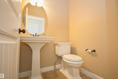 Pedestal sink with an oval mirror, complemented by a white toilet, tile flooring, and a beadboard-paneled door - 11513 17 Avenue, Edmonton, AB 