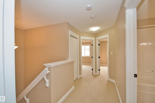 Upper-level hallway with neutral carpeting, white trim, and light beige walls - 11513 17 Avenue, Edmonton, AB 