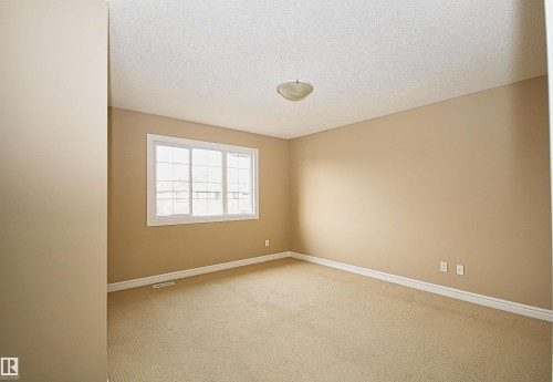 Carpeted room featuring a large window with white framing, neutral-toned walls, and white baseboards - 11513 17 Avenue, Edmonton, AB 