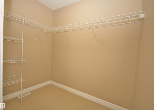 Walk-in closet with carpet flooring, light beige wall paint, white baseboards, and white wire shelving - 11513 17 Avenue, Edmonton, AB 