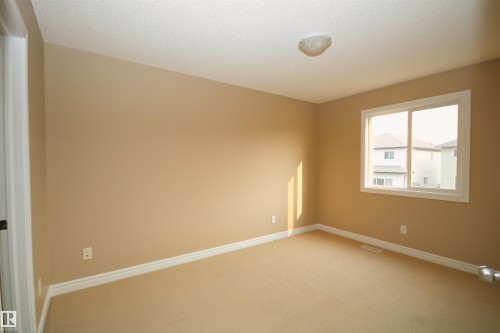 Neutral-toned room featuring a large window with white trim, beige carpeting, and a ceiling-mounted light fixture - 11513 17 Avenue, Edmonton, AB 