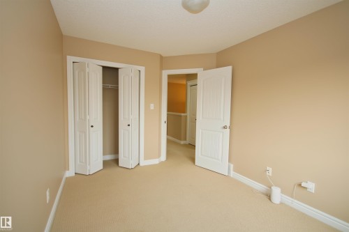 Spacious room featuring neutral paint, carpeted flooring, white bi-fold closet doors, white baseboards, and a white interior door - 11513 17 Avenue, Edmonton, AB 