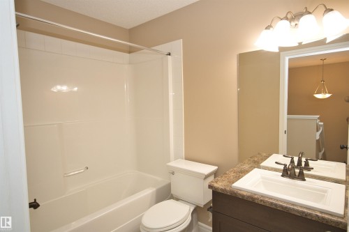 Bathroom featuring a white bathtub/shower combination with a grab bar, a toilet, a vanity with an integrated sink, a dark wood-finish cabinet, and a framed mirror - 11513 17 Avenue, Edmonton, AB 