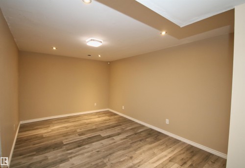 Spacious room featuring wood-finish flooring, neutral wall paint, and white baseboards - 11513 17 Avenue, Edmonton, AB 