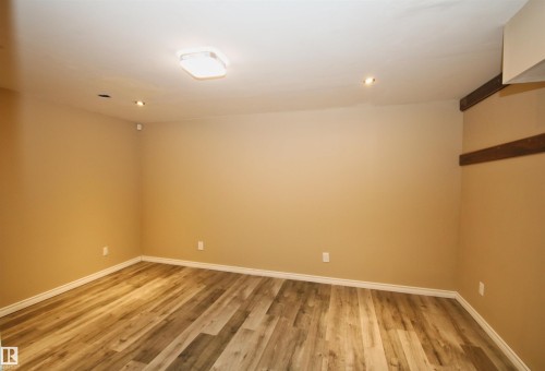 Spacious room featuring wood-finish flooring, neutral-toned walls, recessed lighting, a flush mount ceiling fixture, and white baseboards - 11513 17 Avenue, Edmonton, AB 