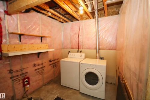 Laundry area featuring a washer and dryer, concrete flooring, exposed ceiling joists, wall-mounted shelving, and insulated walls - 11513 17 Avenue, Edmonton, AB 