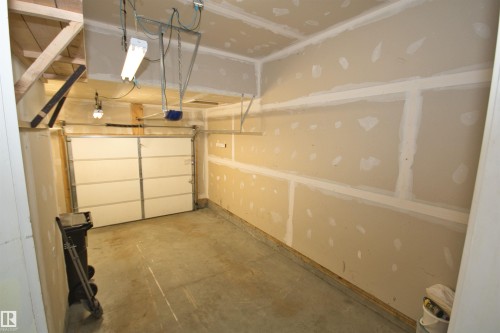 Single-car garage featuring a paneled overhead door, concrete flooring, and unfinished drywall walls - 11513 17 Avenue, Edmonton, AB 
