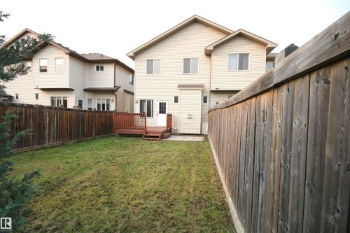 Expansive backyard featuring a stained wood deck, a white door providing exterior access, and surrounding wood fencing - 11513 17 Avenue, Edmonton, AB 