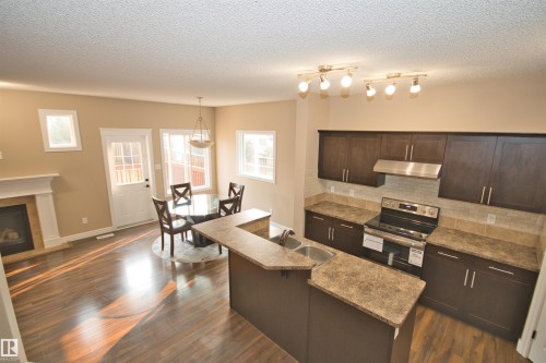 Kitchen and dining area featuring dark wood-finish cabinetry, stainless steel appliances, a breakfast bar with a double basin sink, light-colored countertops, and wood-finish flooring - 11513 17 Avenue, Edmonton, AB 