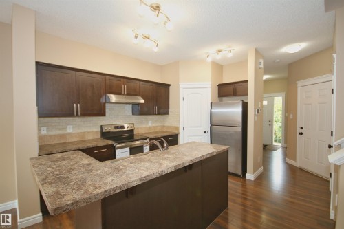 Kitchen featuring rich wood-finish cabinetry, stainless steel appliances, a tiled backsplash, and an island with a breakfast bar - 11513 17 Avenue, Edmonton, AB 