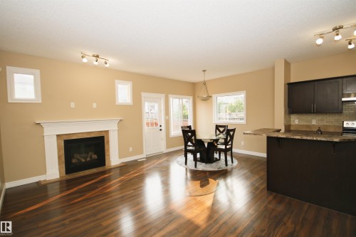 Open-concept living area featuring rich wood-finish flooring, a white mantel fireplace with a tile surround, and multiple windows - 11513 17 Avenue, Edmonton, AB 