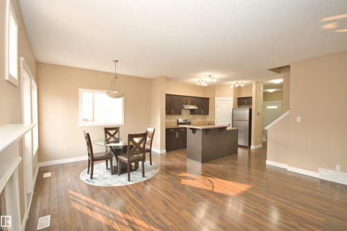 Open-concept living space featuring wood-finish flooring, a contemporary kitchen, and a dining area with pendant lighting - 11513 17 Avenue, Edmonton, AB 